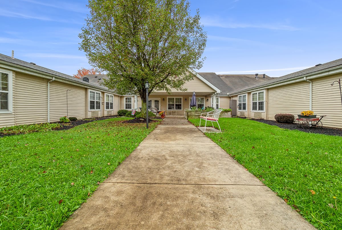 A view of a cozy house with a lush green lawn and a central pathway leading to the entrance.