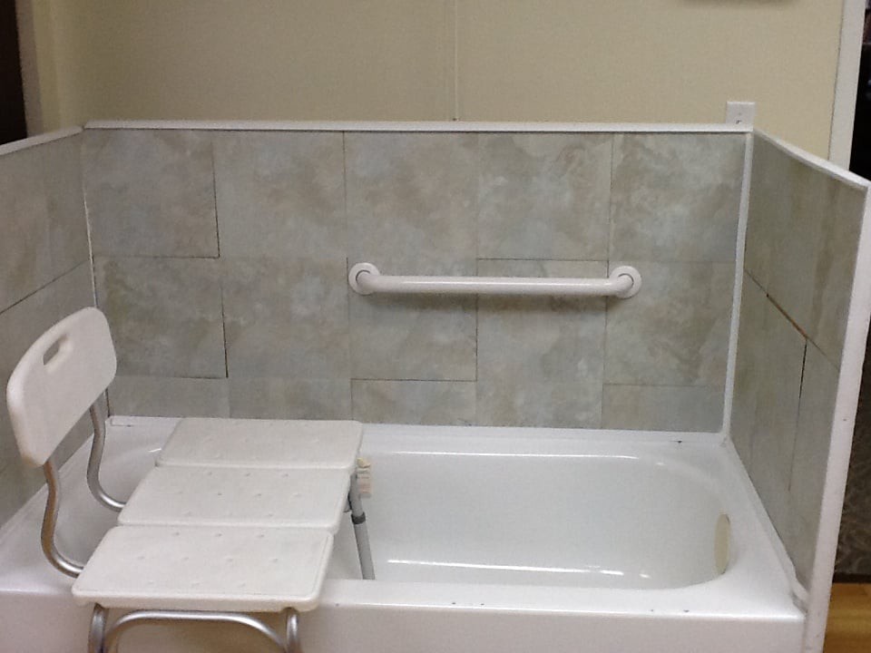 A bathroom featuring a bathtub with a grab bar for accessibility and safety, surrounded by tiled walls.