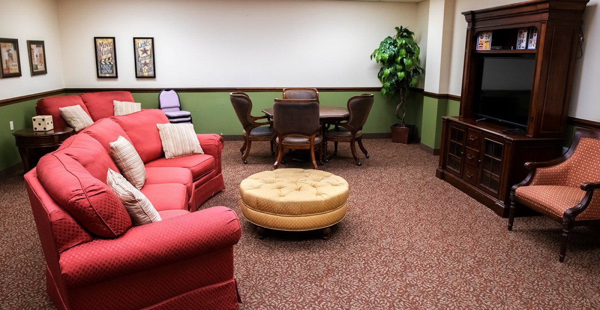 A cozy living room with a red sofa and round ottoman, accompanied by a dining table and chairs.