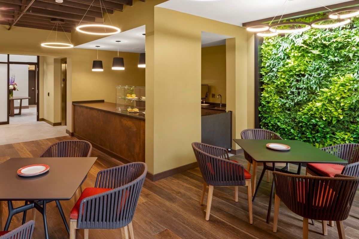 A modern cafe interior featuring comfortable seating, a green wall, and stylish lighting.