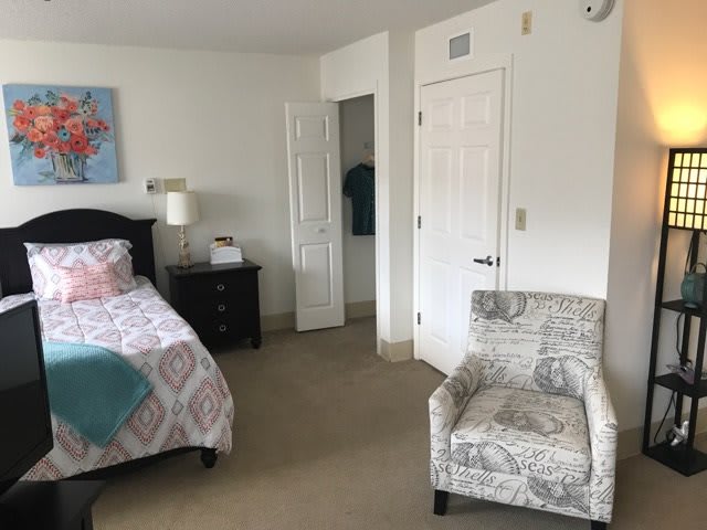 A minimalist bedroom with a bed, armchair, nightstand, and an open door.