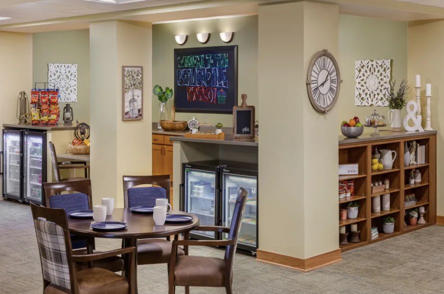 A cozy dining area with elegant table settings and stylish decor, featuring a wall clock, artwork, and mini refrigerators.