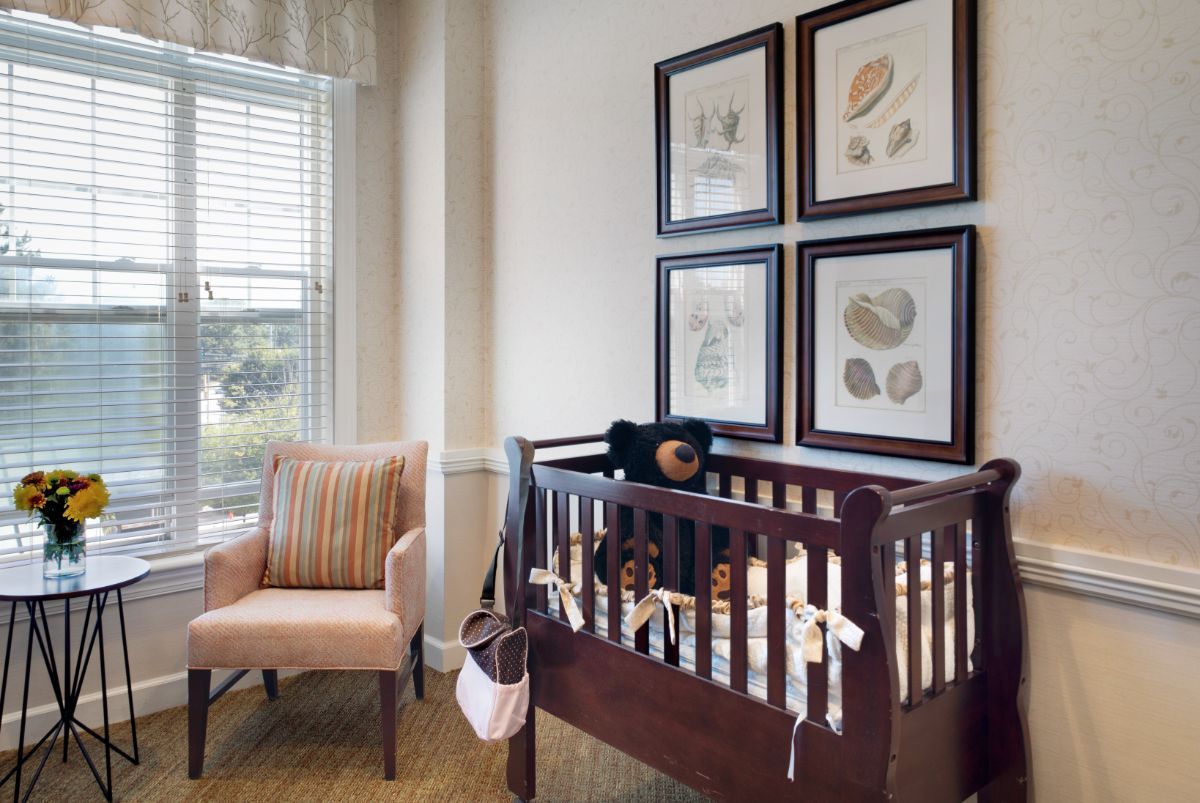 A cozy nursery featuring a crib with a teddy bear, a comfortable chair, and decorative framed art on the wall.
