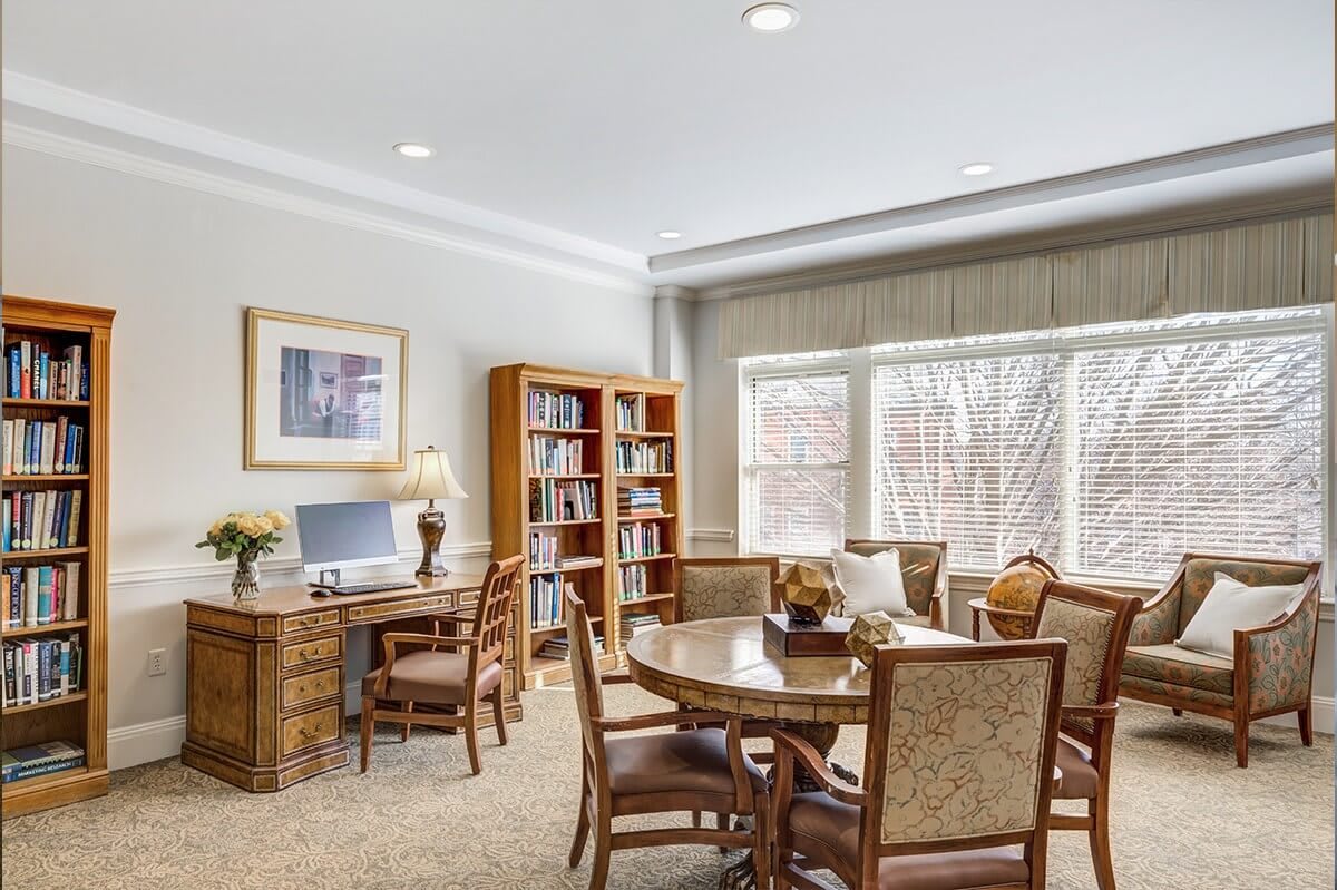 A cozy office space with a desk, bookshelf, and round table surrounded by chairs.