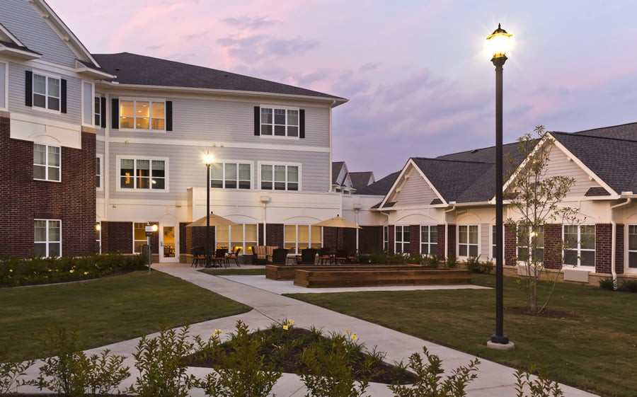 A well-lit exterior view of a modern building with a courtyard and landscaped grounds at dusk.
