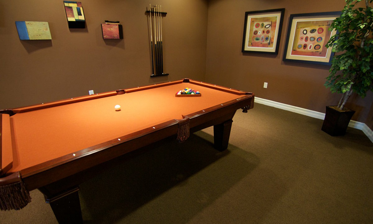 A cozy game room featuring a billiards table with orange felt, surrounded by framed art on the walls.
