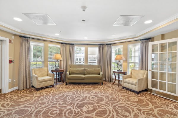 A cozy living room setup with a sofa, two armchairs, and decorative lamps on tables by the windows.