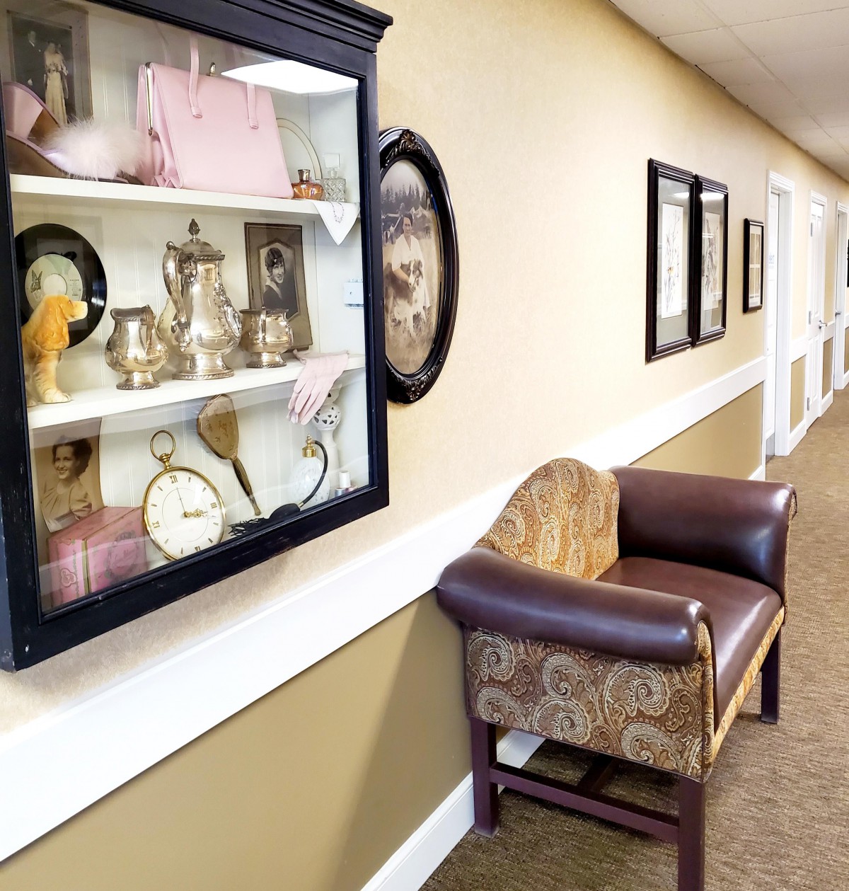 A hallway with a display case of antiques and a vintage chair along the wall.