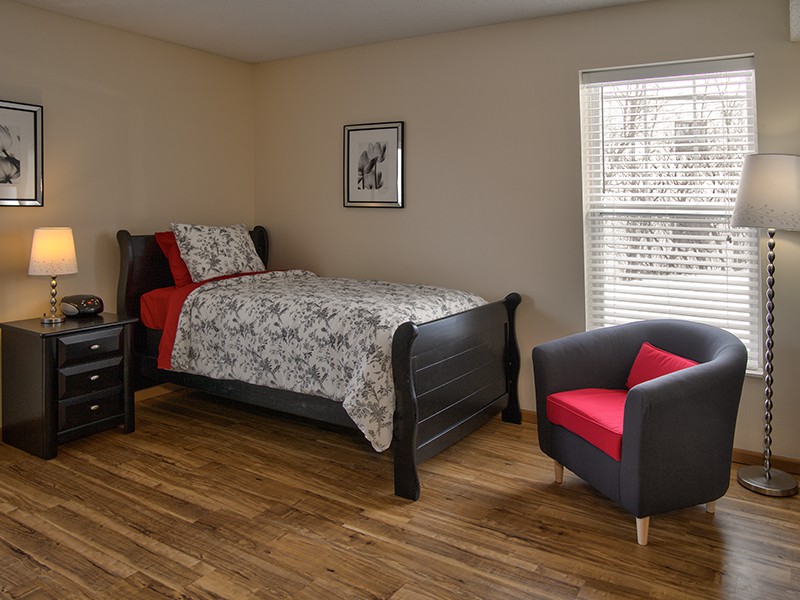 A minimalist bedroom with a single bed and a comfortable chair on a wooden floor.