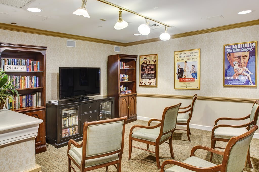 A cozy living room setup with chairs arranged facing a television and bookshelves, illuminated by overhead lighting.