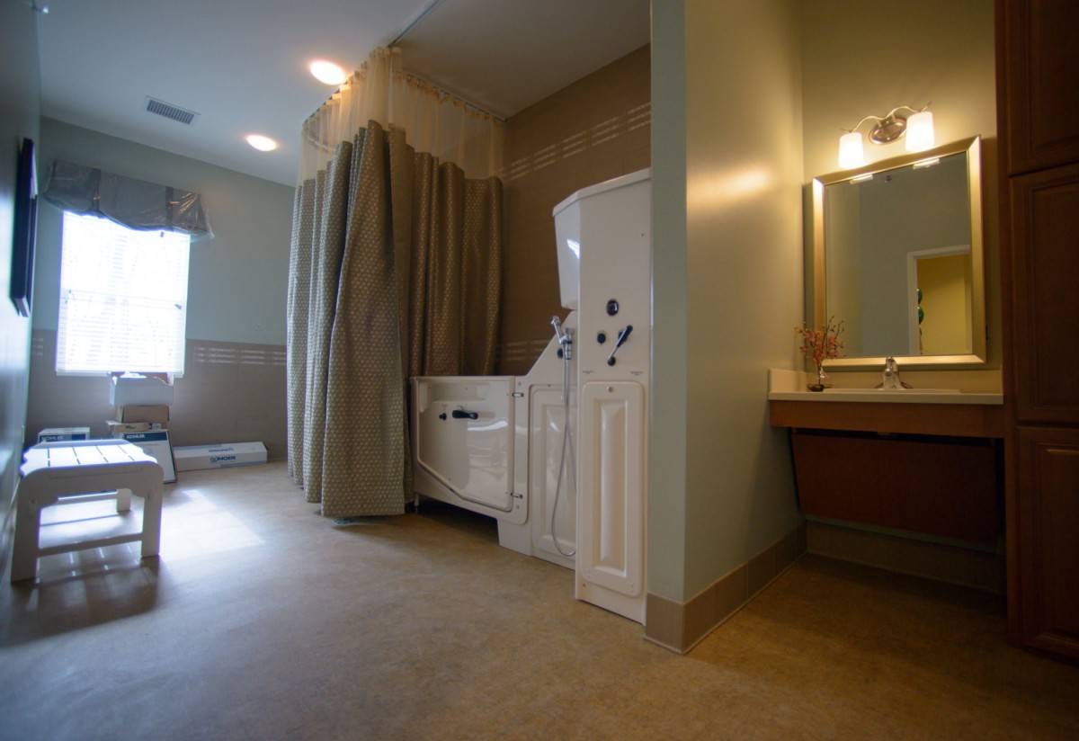 An accessible bathroom featuring a walk-in tub with curtains, tiles, and a mirrored vanity area.