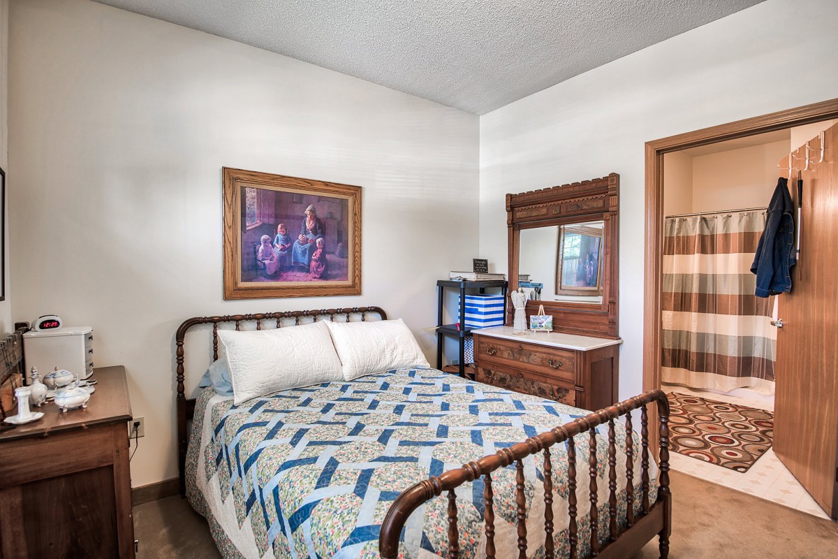 A cozy bedroom with a metal-frame bed and quilt, featuring a wooden dresser and mirror.