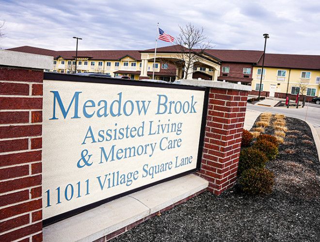 Sign for Meadow Brook Assisted Living & Memory Care facility with building in the background.