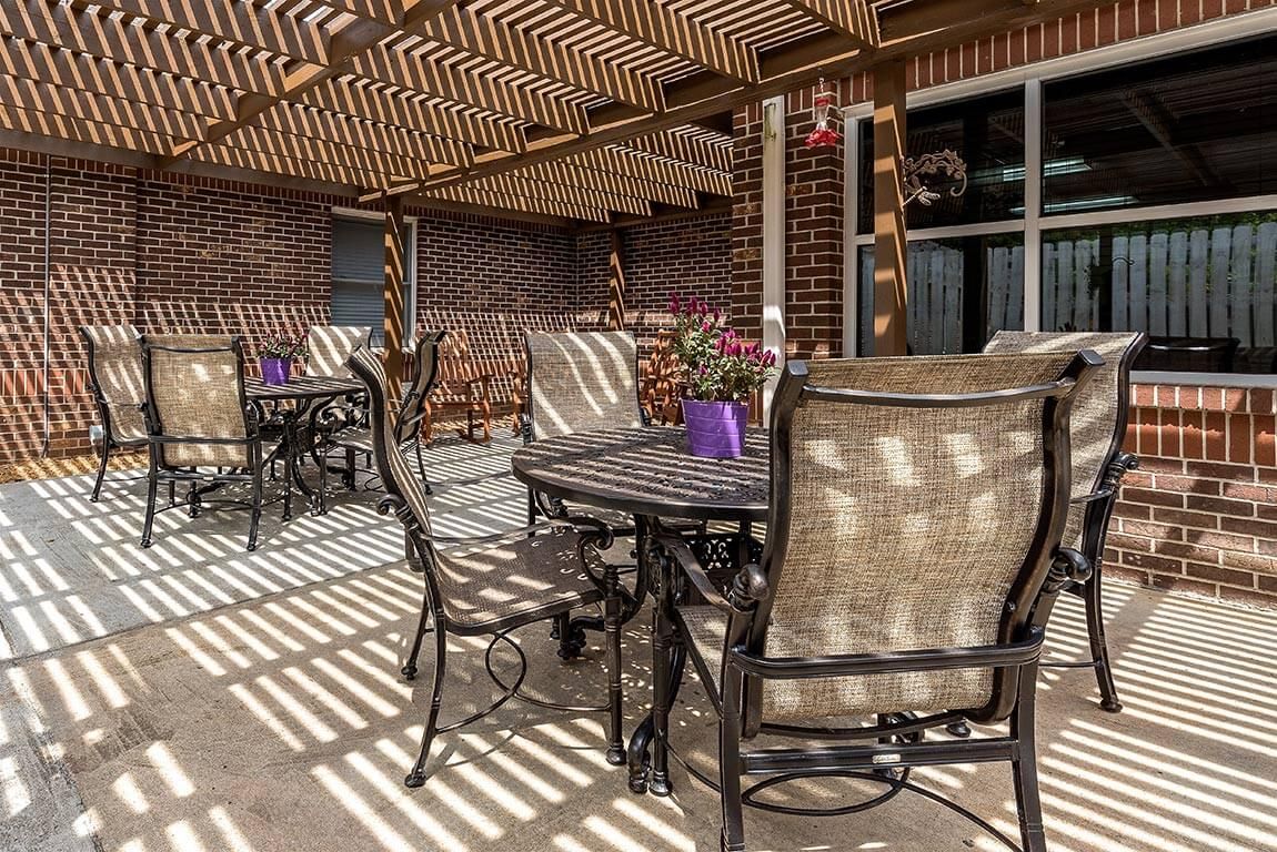 An inviting patio area with a pergola casting striped shadows over outdoor furniture and potted plants.