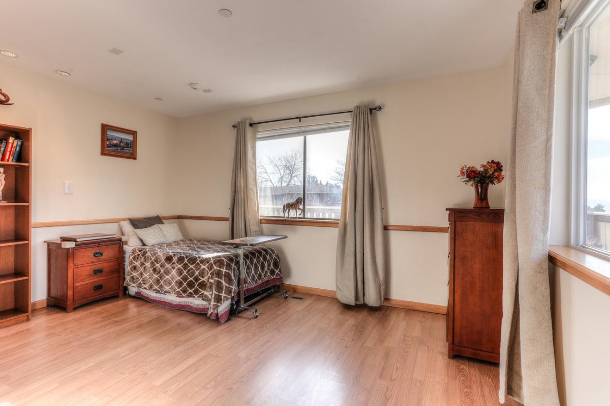 A cozy bedroom with a bed, wooden dresser, and large window with curtains.