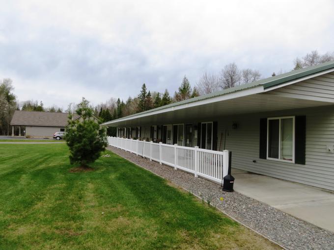 A spacious house with a long porch and white fence, surrounded by a green lawn and trees under an overcast sky.