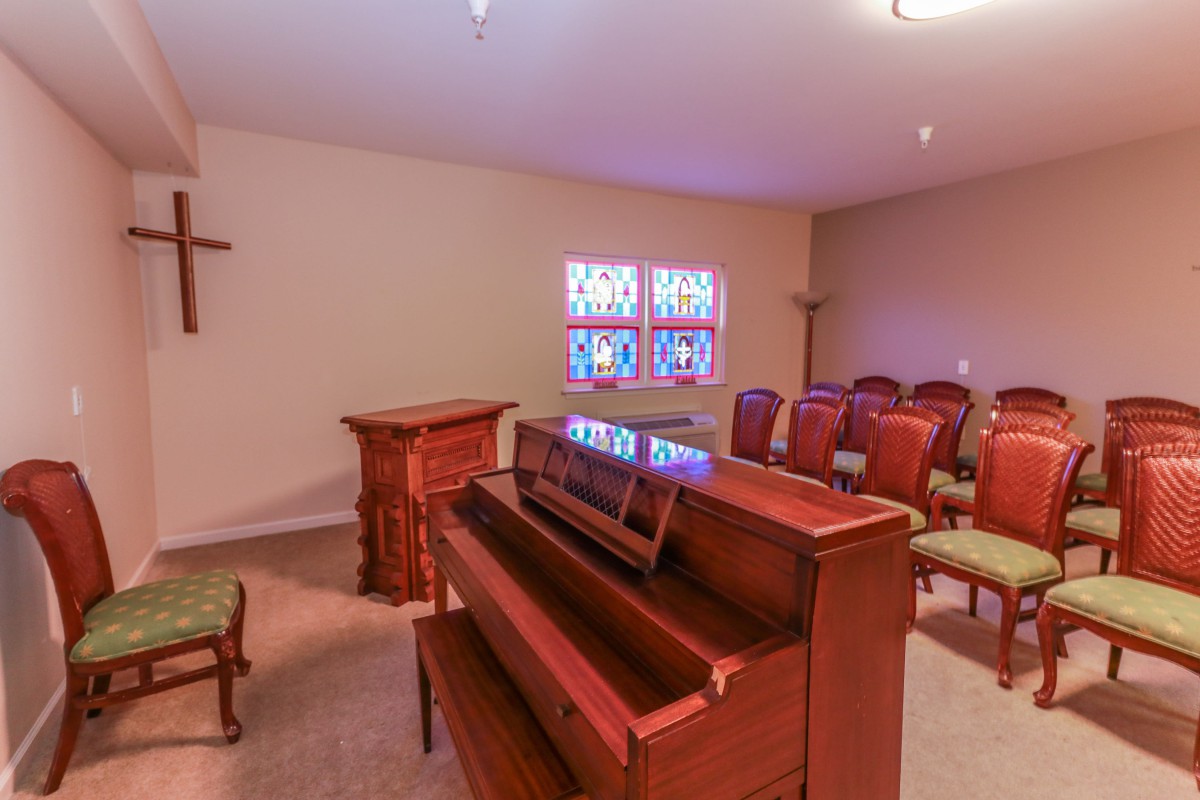 A small chapel interior with a piano, seating, and stained glass windows.