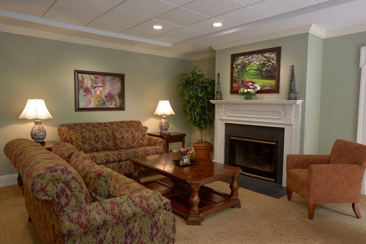 A cozy living room with a traditional design, featuring comfortable sofas, a wooden coffee table, and a fireplace adorned with artwork.