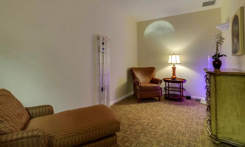 A cozy living room featuring comfortable chairs, a side table with a lamp, and warm lighting.