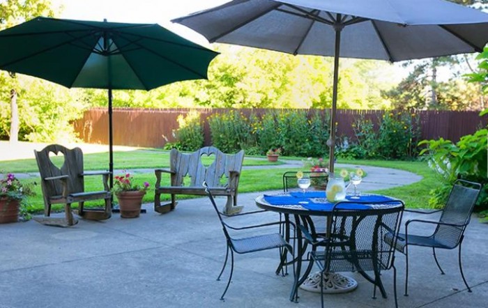 A cozy patio with outdoor seating, shaded by umbrellas, overlooking a lush garden.