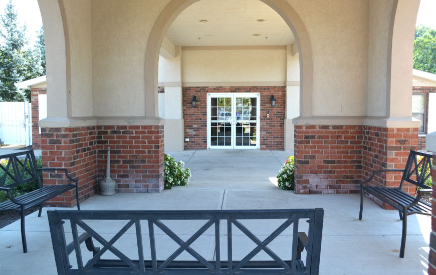 A bench positioned under an archway leading to a doorway with brick walls and plants on either side.