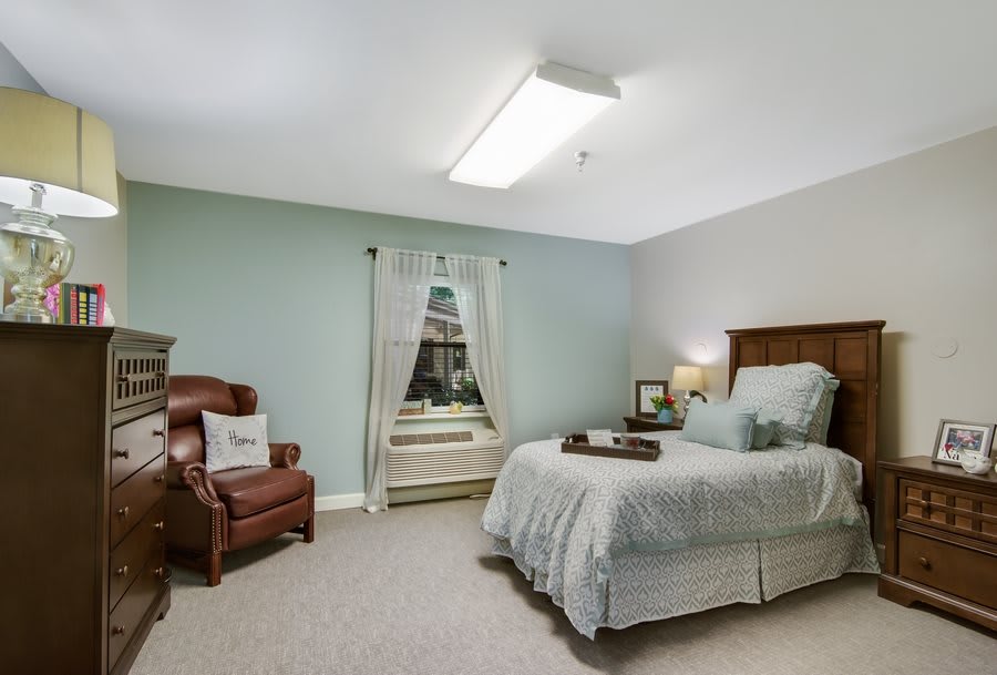 A cozy bedroom with a bed, a leather chair, and a window.