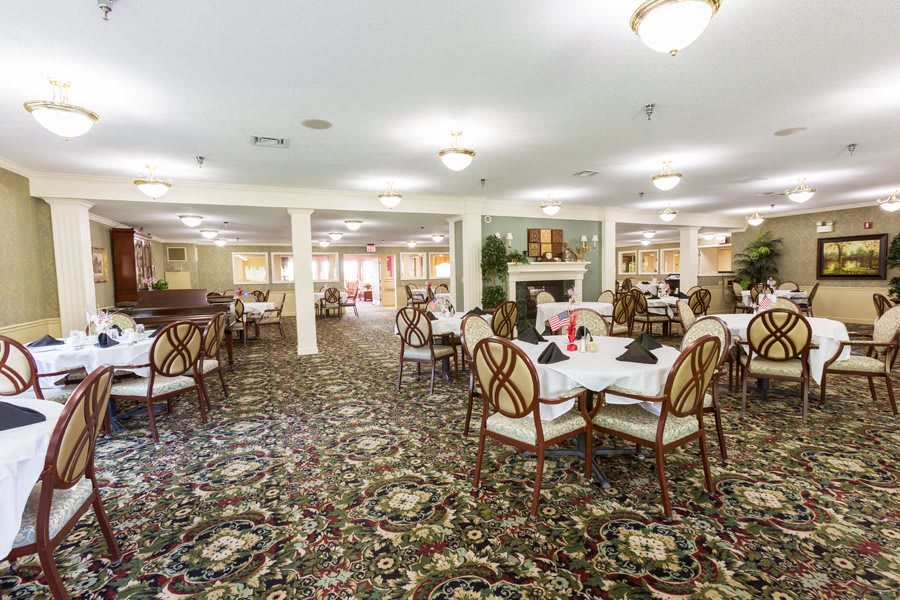 A spacious dining room with elegantly set tables and chairs, featuring warm lighting and decorative carpeting.