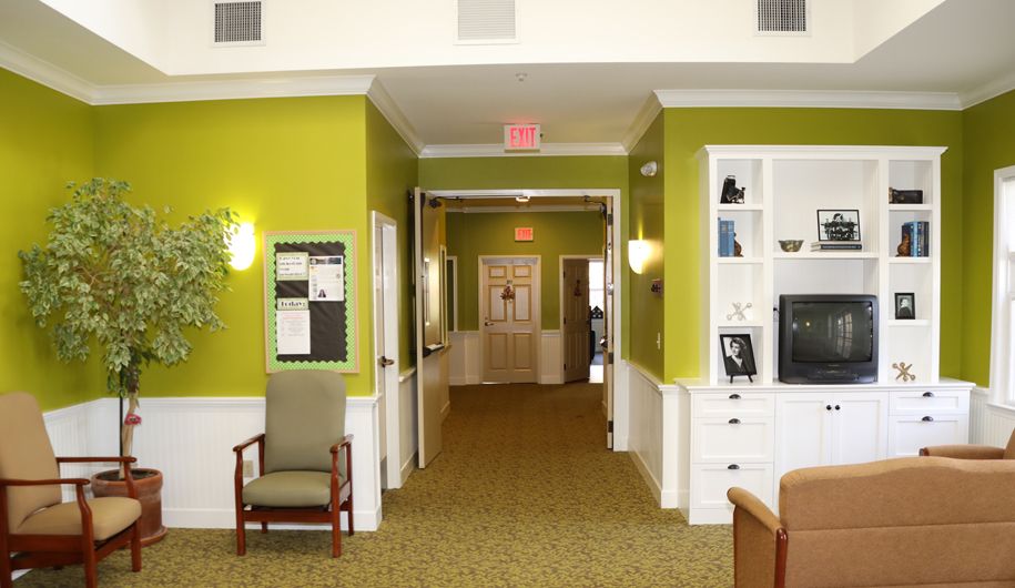 A well-lit hallway with green walls and carpeted flooring, featuring furniture and an exit sign.