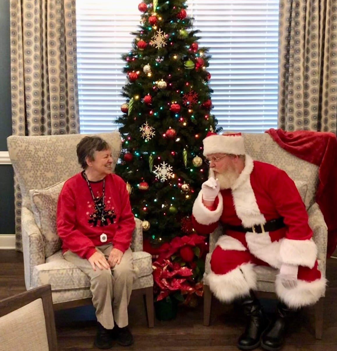A child sits next to Santa Claus by a decorated Christmas tree, enjoying the holiday spirit.