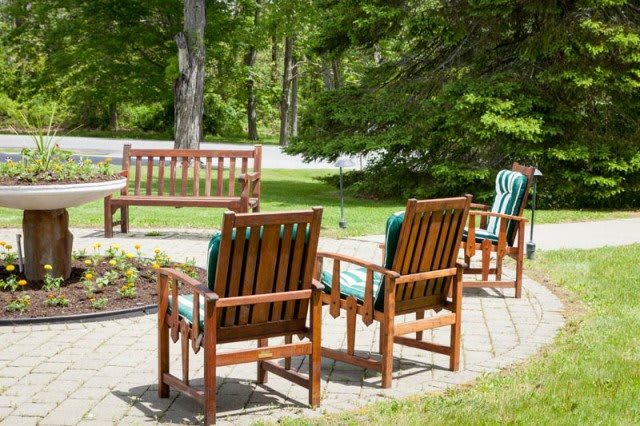 A peaceful garden patio with wooden chairs and a bench surrounded by greenery.