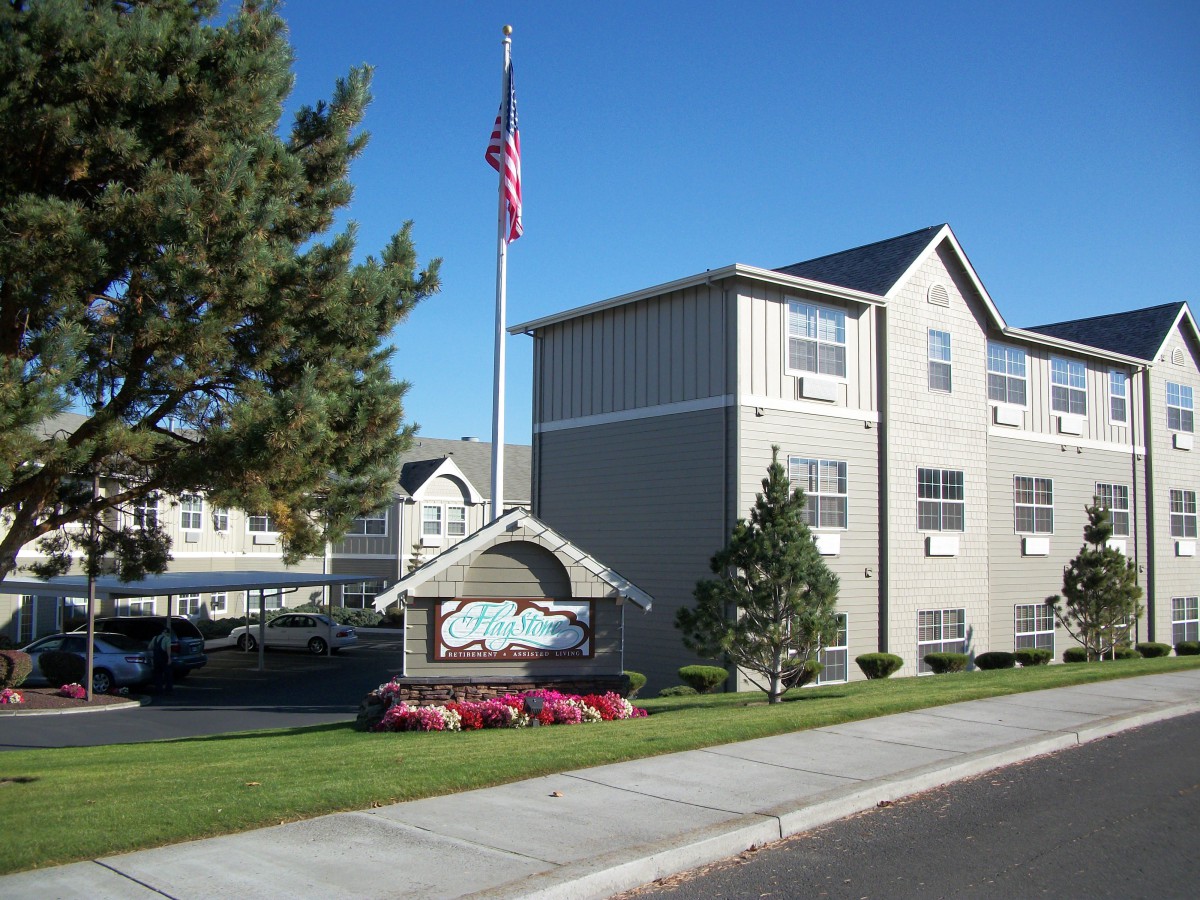 An apartment complex with an American flag and well-maintained landscaping on a clear day.
