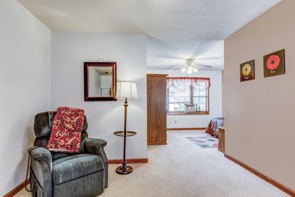 A cozy living room with a comfortable chair, mirror, and lamp, leading to a bedroom area with natural light from a window.