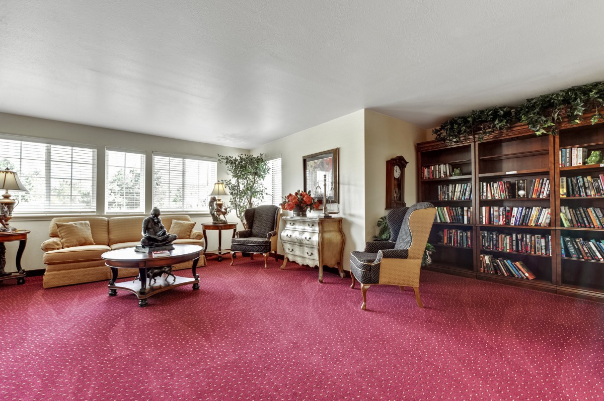 A spacious living room featuring a red carpet, comfortable seating, and a well-stocked bookshelf.