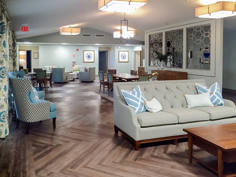 A spacious and elegantly designed living room featuring comfortable sofas, armchairs, and stylish lighting fixtures on a hardwood floor.