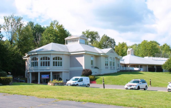 A large building with arched windows, surrounded by cars and greenery on a sunny day.
