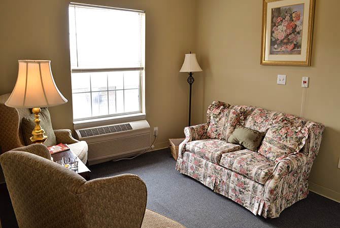 A cozy living room with a floral sofa, floor lamp, and a large window.