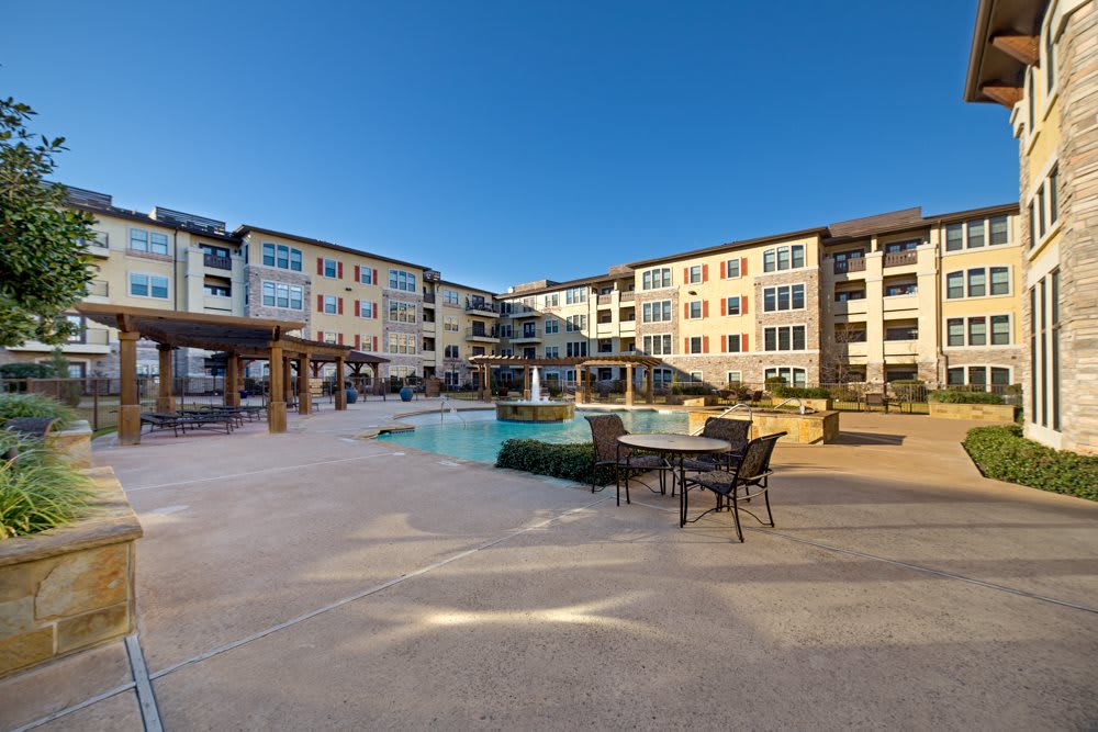 A modern apartment complex with a swimming pool and outdoor seating area under a clear blue sky.