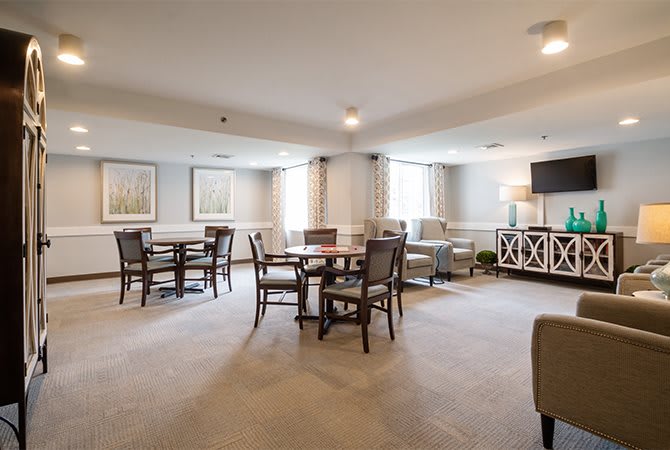 A spacious living room with tables and chairs, featuring large windows and elegant decor.
