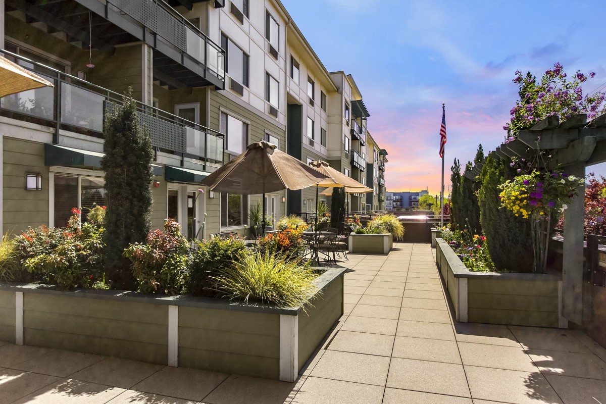 A modern apartment building with a well-maintained patio and lush green plants at sunset.