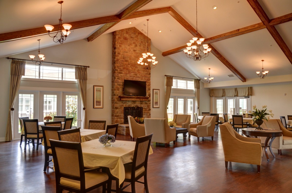A cozy dining room with high ceilings, featuring a brick fireplace, chandeliers, and elegantly set tables and chairs.
