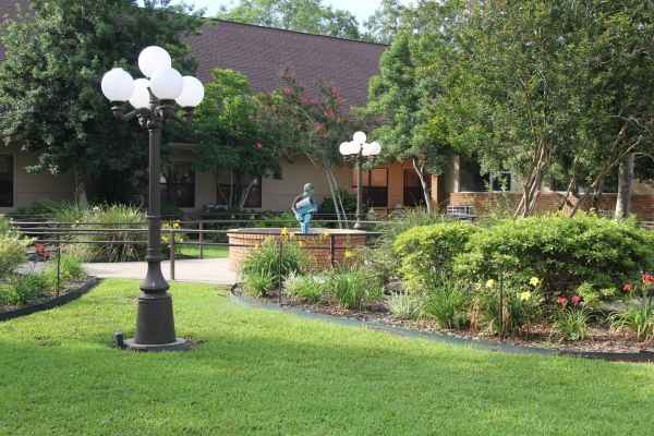 A serene garden scene with a lamp post, lush greenery, and a central statue.
