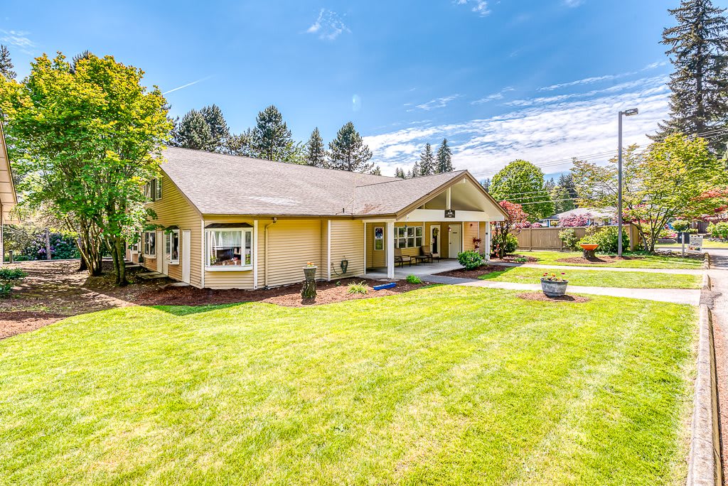 A suburban house with a spacious green lawn and trees under a clear blue sky.