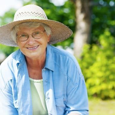 A senior woman smiling while gardening outdoors on a sunny day.