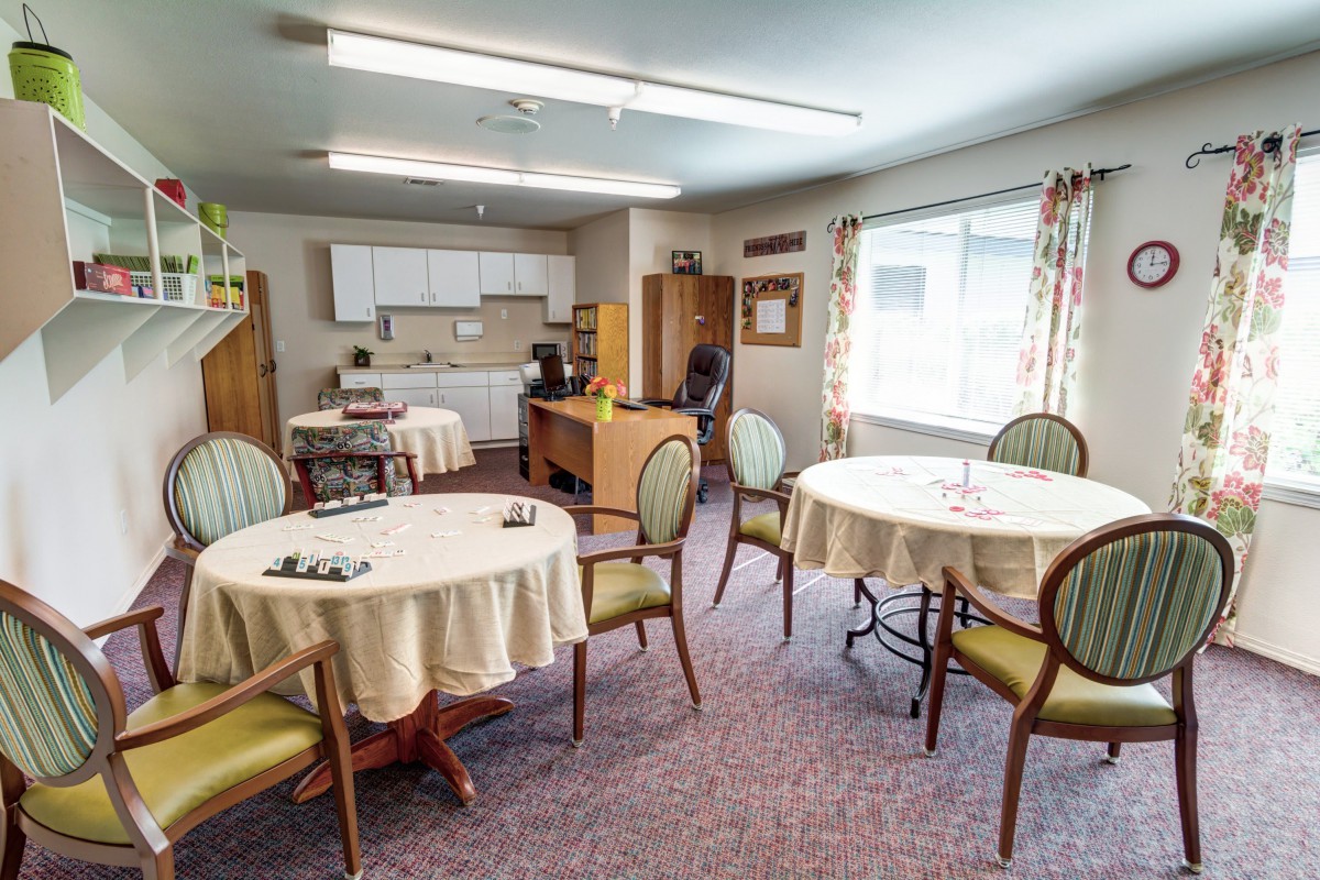 A cozy dining area with multiple round tables, chairs, and a small kitchen space in the background.