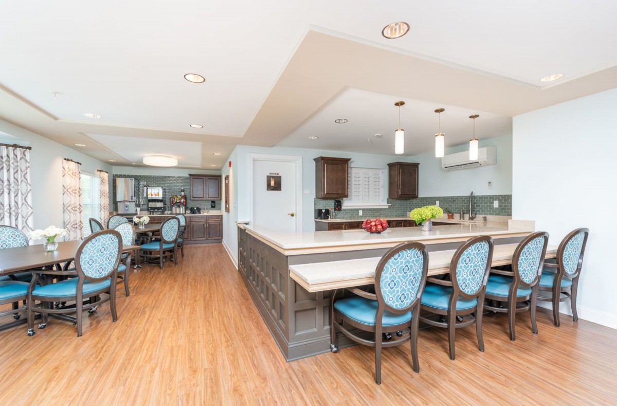 A modern kitchen and dining area with an open layout, featuring wood flooring, bar stools at the counter, and contemporary lighting fixtures.