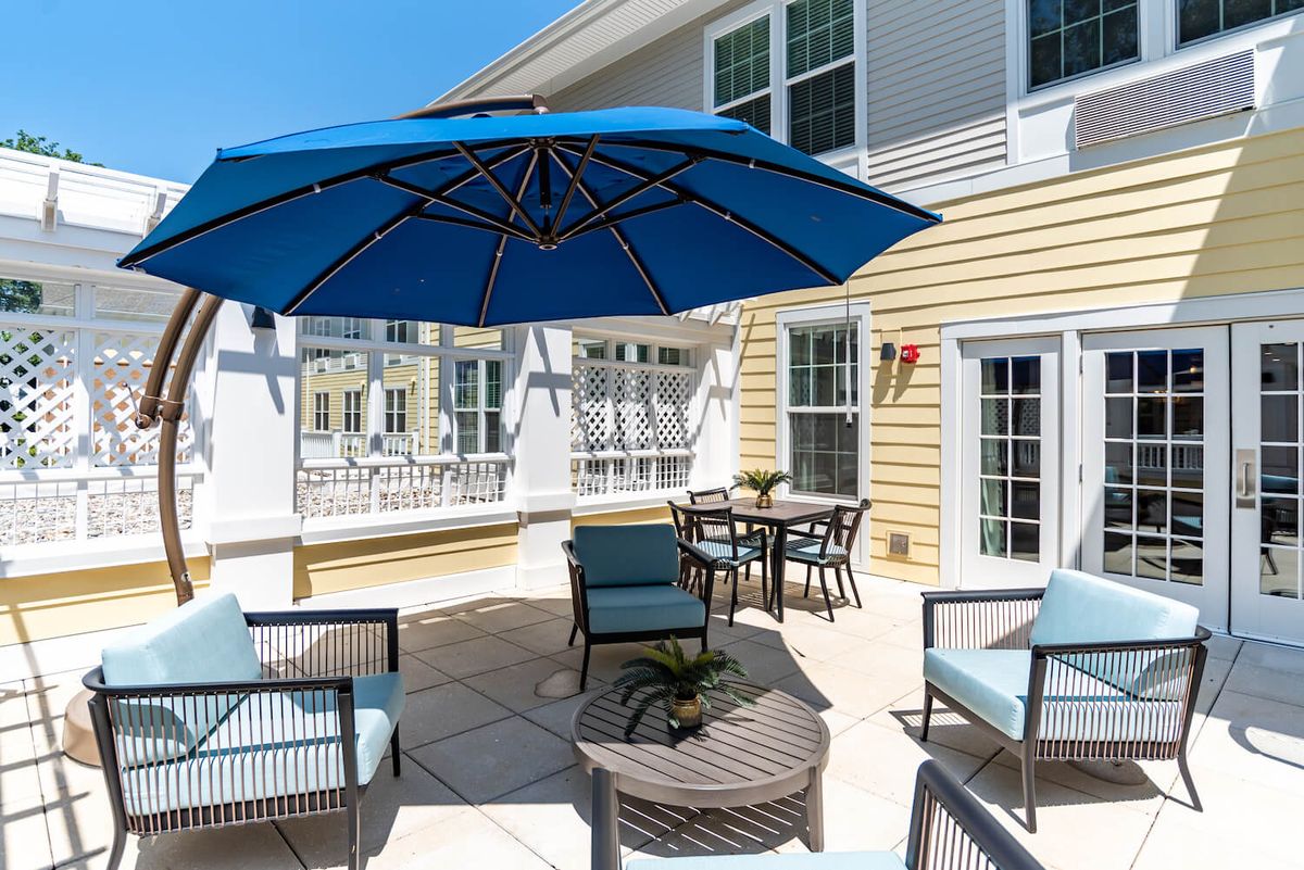 A sunny outdoor patio with a blue umbrella, comfortable seating, and a dining table.