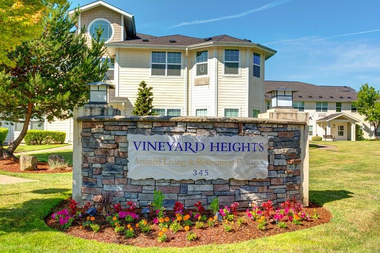 The entrance sign for Vineyard Heights apartment complex with a view of the residential building and landscaped flowers.