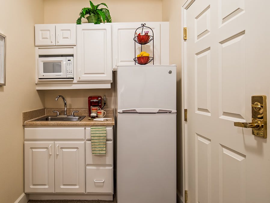 A compact kitchen with white cabinets, a refrigerator, and a microwave.