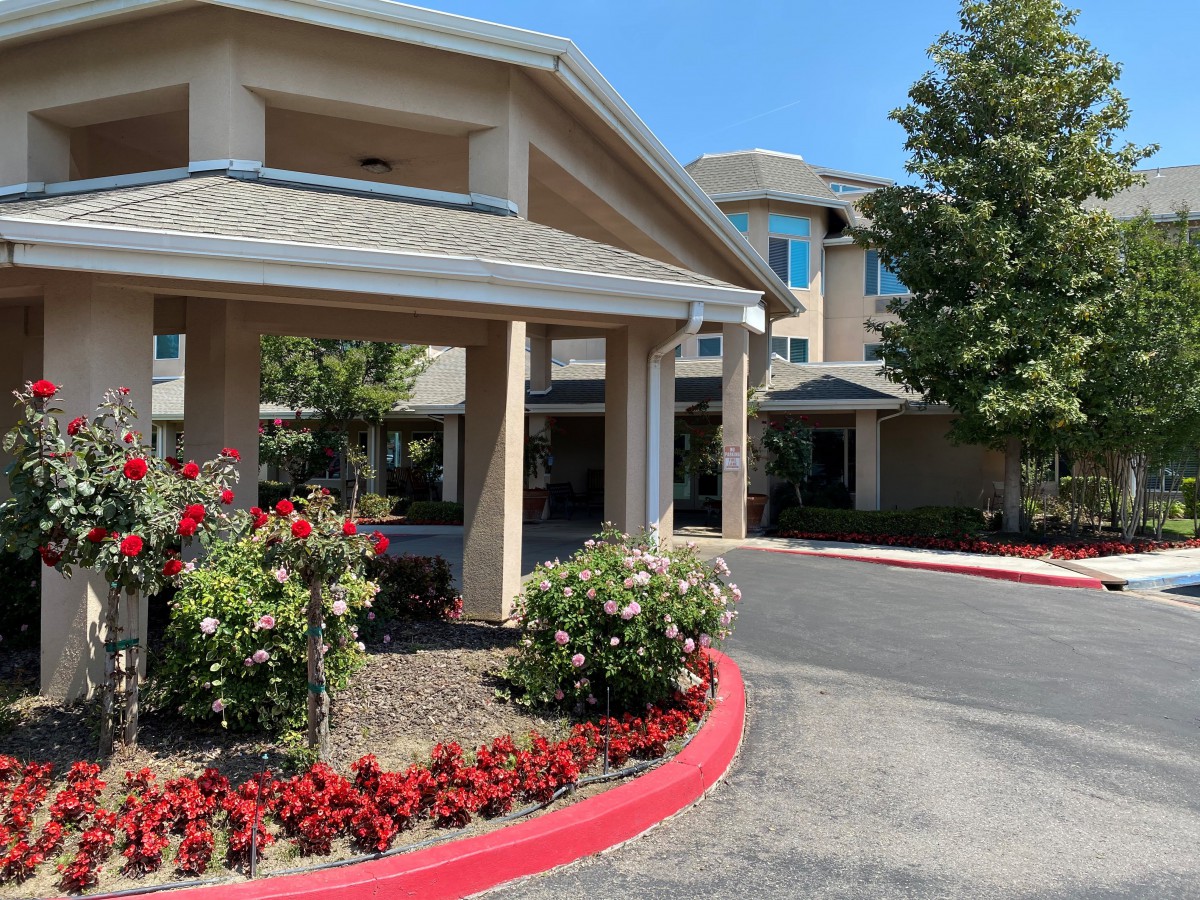 The entrance of a building with landscaped flowers and trees along the driveway.