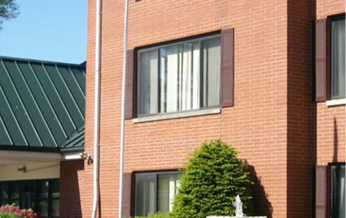A brick building with windows and a neatly trimmed shrub in front.
